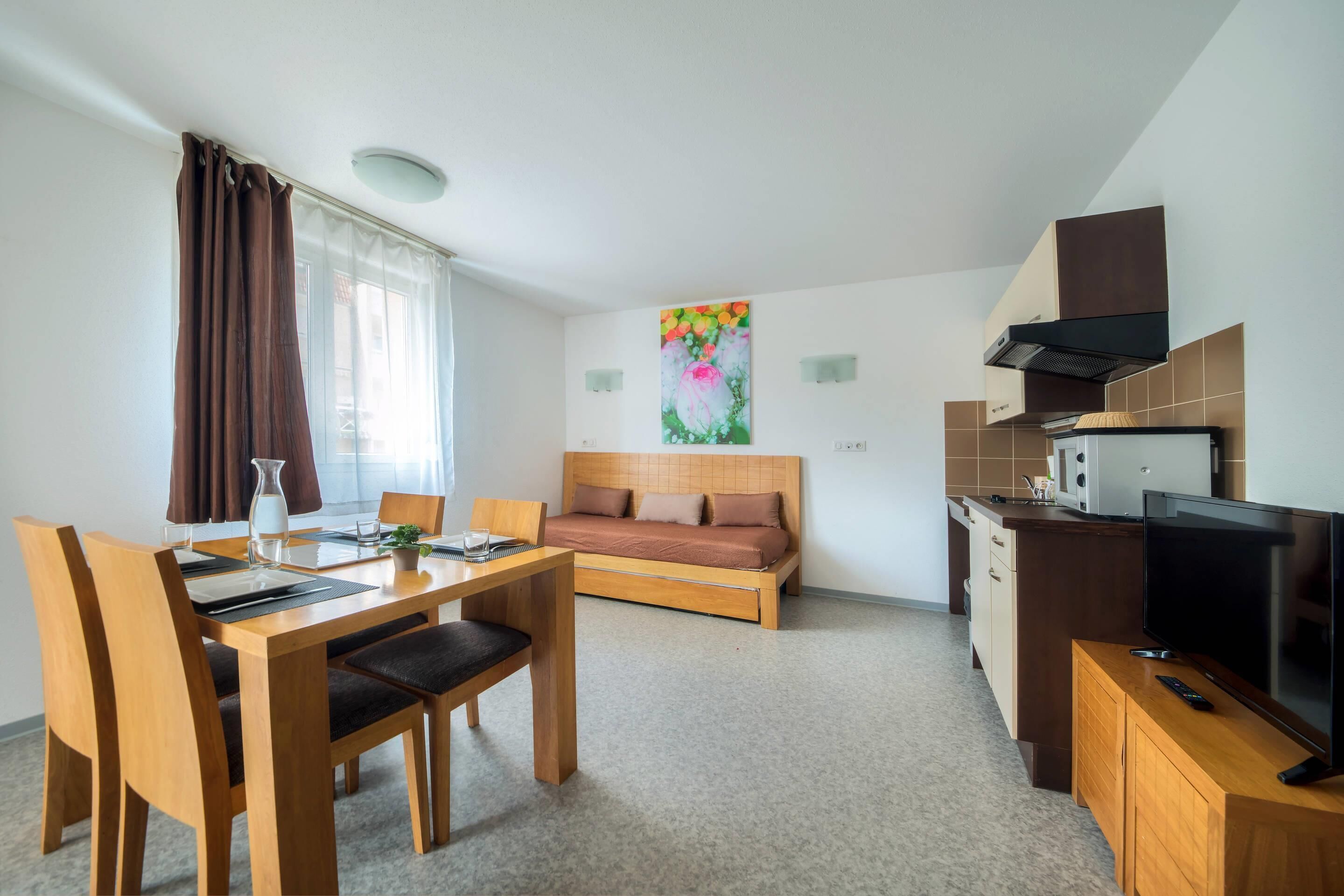 Un espace de vie compact comprenant un coin repas, un canapé, une kitchenette et un téléviseur.