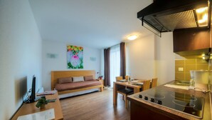 Una habitación de hotel moderna con una cama de madera, una mesa de comedor con sillas, una zona de cocina con estufa y un cuadro en la pared.