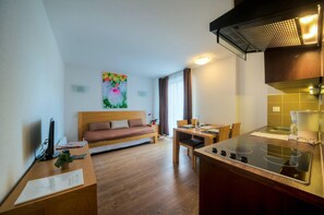 Una habitación de hotel moderna con una cama de madera, una mesa de comedor con sillas, una zona de cocina con estufa y un cuadro en la pared.