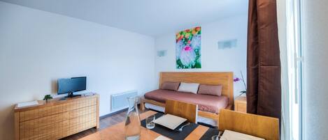 Habitación de hotel moderna con una cama de madera, un televisor sobre un mueble de madera, una mesa de comedor con un jarrón de flores y un cuadro en la pared.