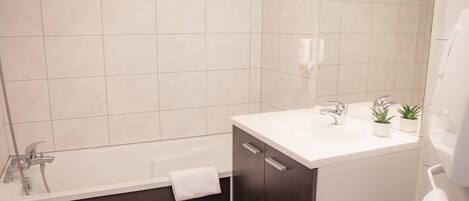 A modern bathroom with a bathtub, a white sink with a mirror, and a small potted plant on the counter.