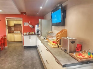 Una cocina de hotel con un sistema de buffet, que incluye un refrigerador, una cafetera y un televisor montado en la pared.