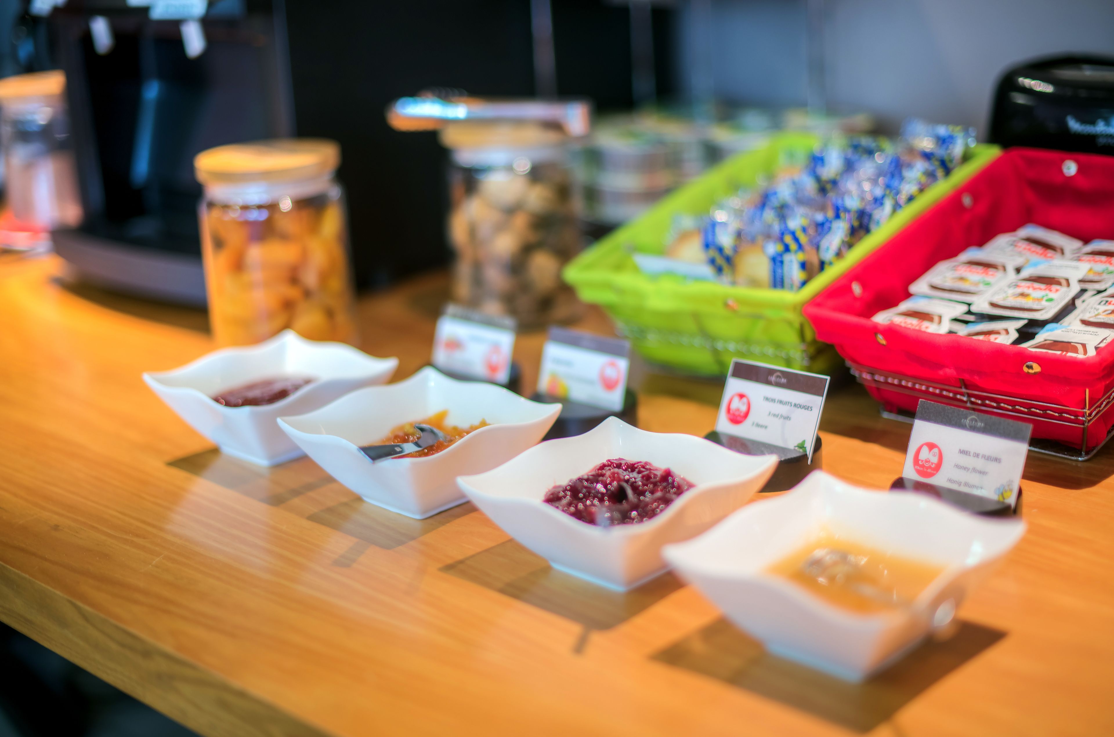A buffet with various food items in bowls and containers, including jams, fruits, and packaged snacks.