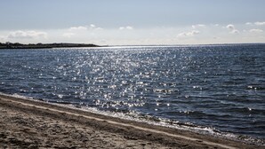 En strand med sandet bredde og roligt vand der spejler sollys.
