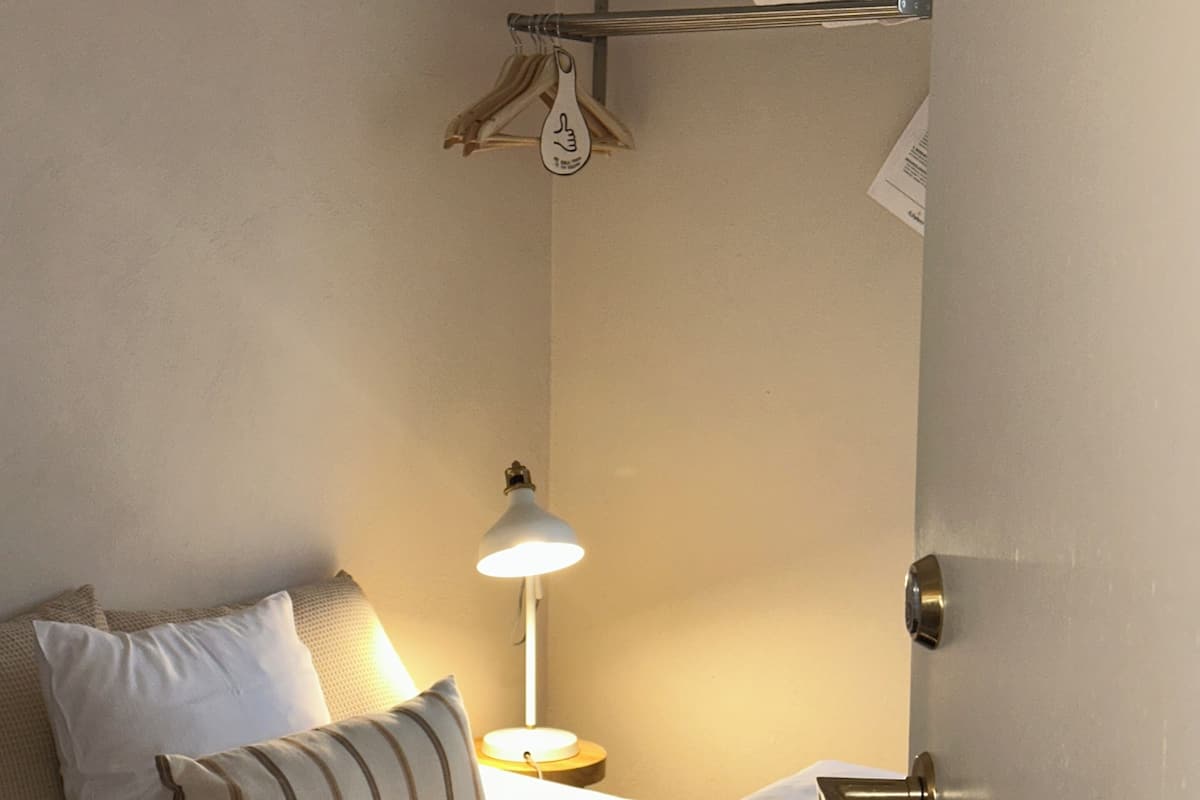A single bed with white bedding, a bedside lamp, and a towel rack above the bed.