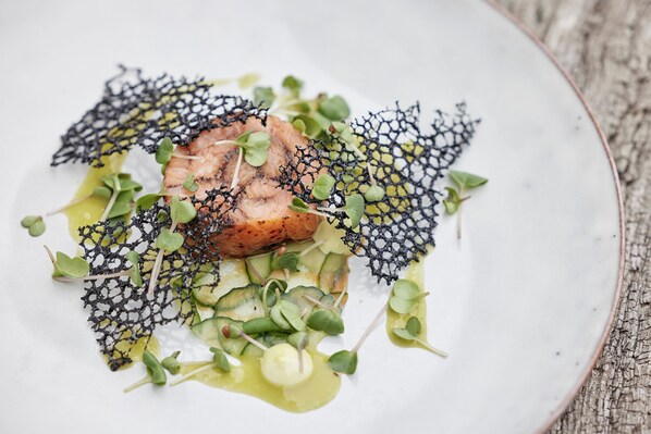 A plate of food with a piece of meat, greens, and a black net-like garnish. - (Haarby)