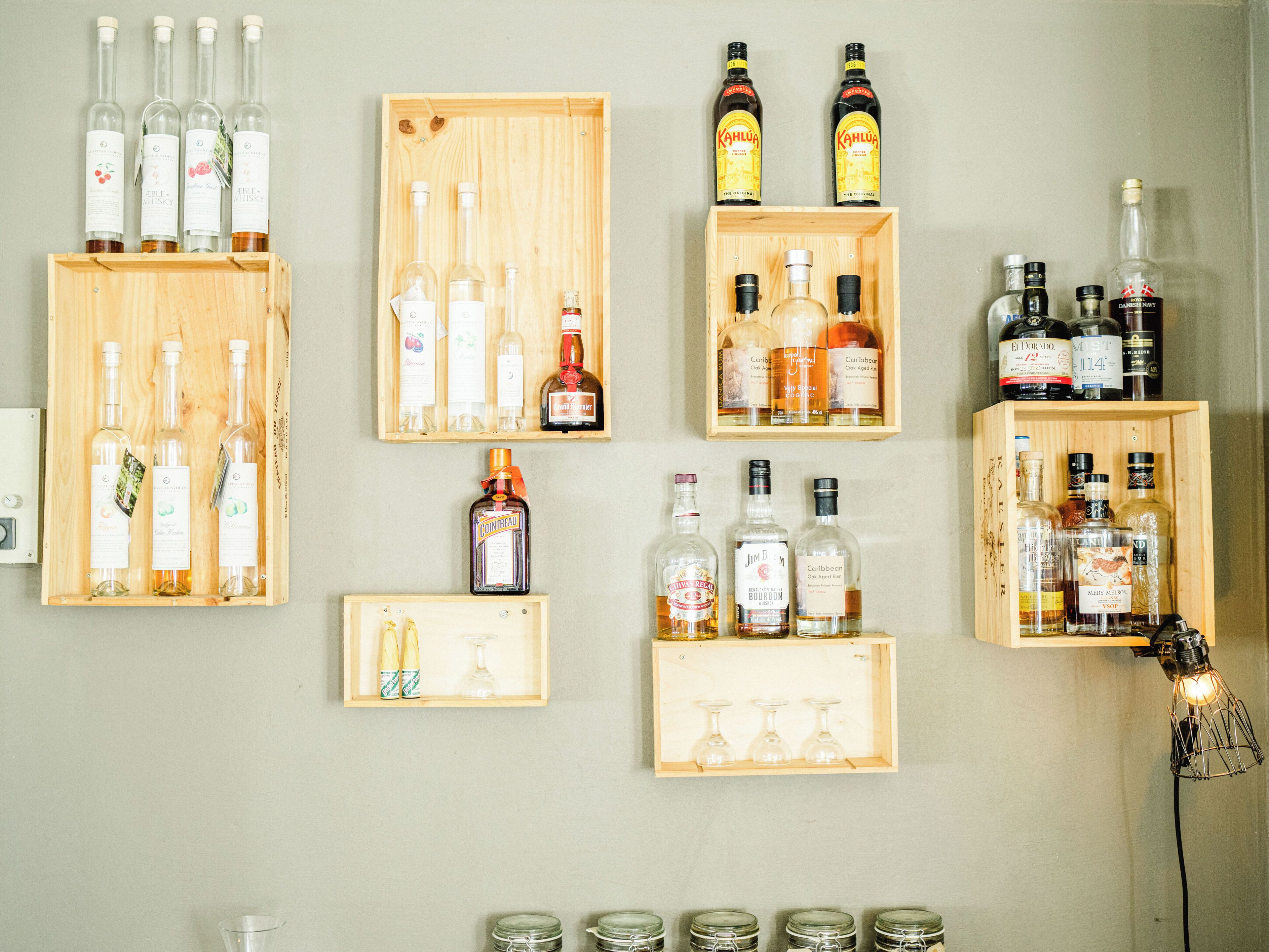 A wall with multiple wooden shelves displaying various bottles of alcohol.
