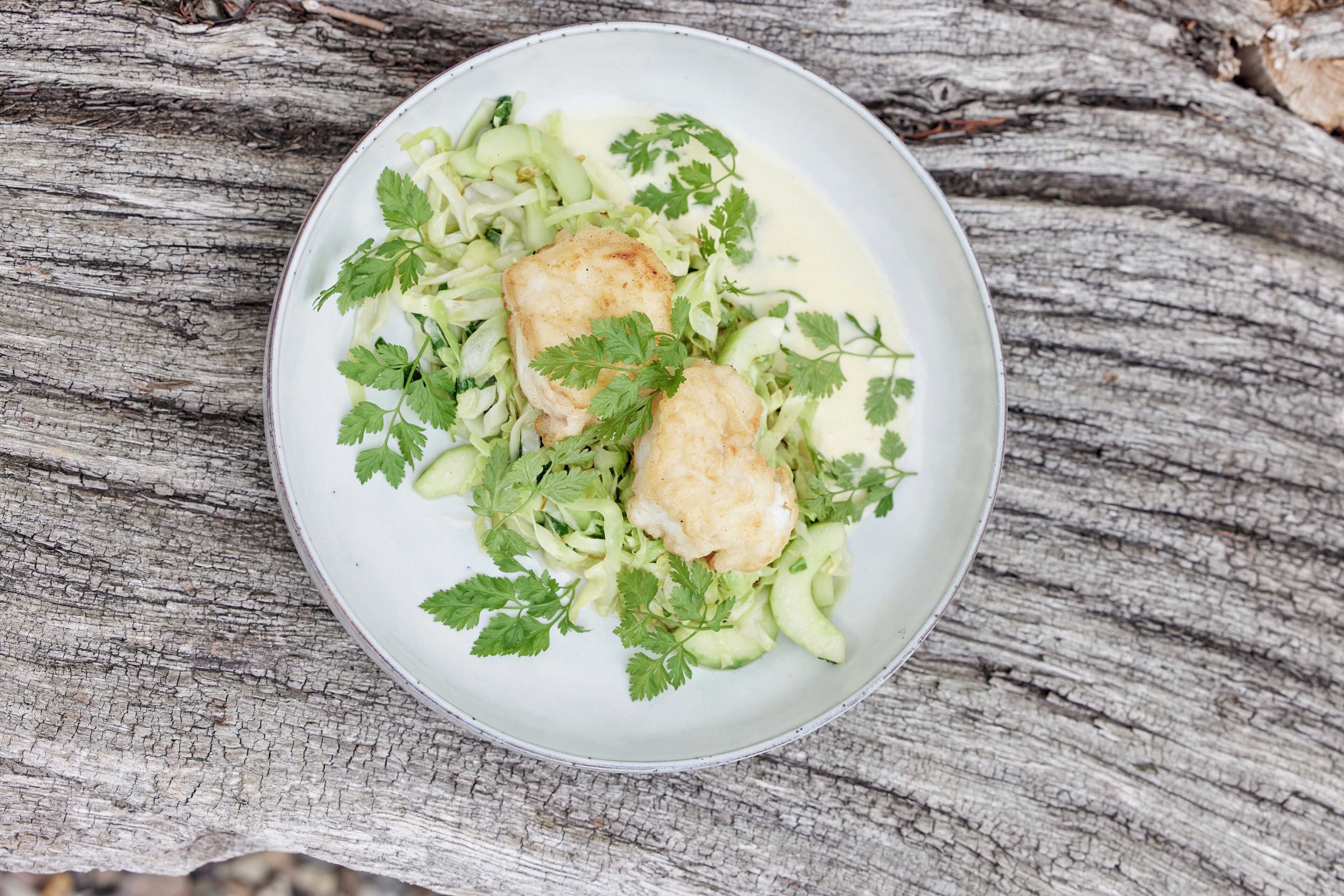 Ein Teller mit Fisch und Gemüse auf einer Holztischplatte.