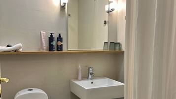 A bathroom with a white toilet, a sink with a mirror above it, and toiletries on a shelf.