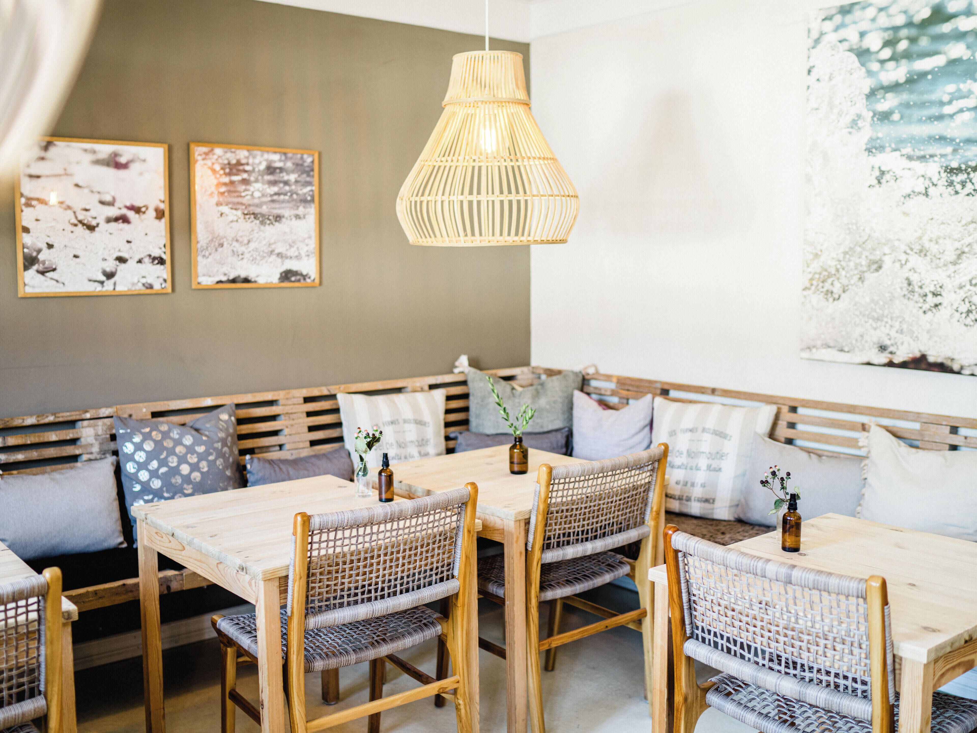 Een eethoek met een houten bank en tafels, rieten stoelen en een hanglamp.