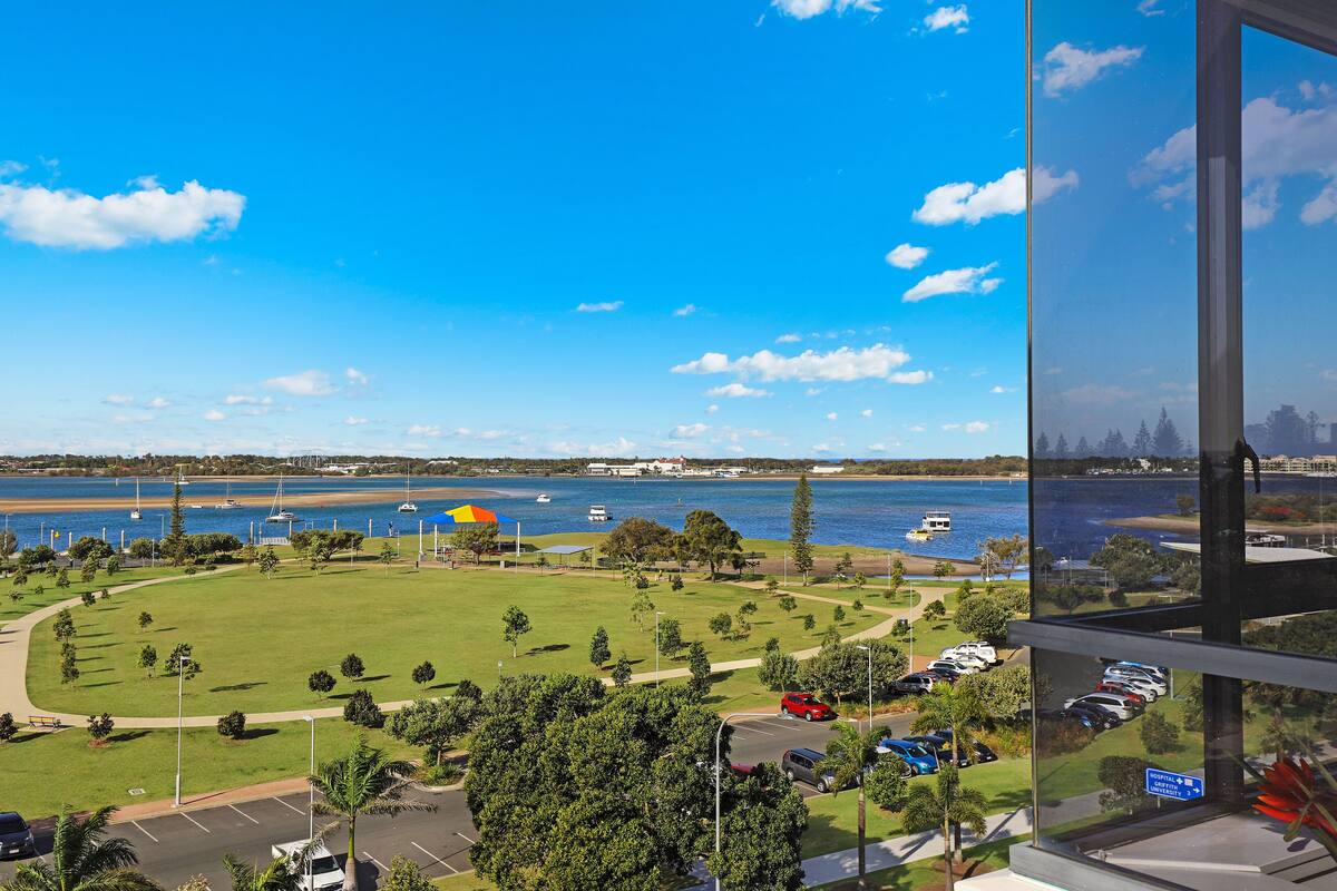 A view from a high-rise window overlooking a park with a lake, boats, and a distant city skyline.