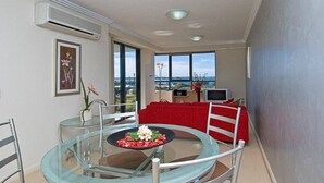A dining area with a glass table, chairs, and a red sofa. There is a TV and a window with a view. - Aqualine Apartments (Southport)