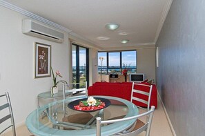 Un comedor con mesa de vidrio, sillas y sofá rojo. Hay un televisor y una ventana con vistas.