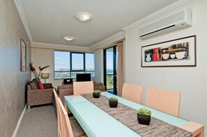 Una sala de estar moderna con una mesa larga, asientos cómodos, un ventanal grande y un equipo de aire acondicionado.