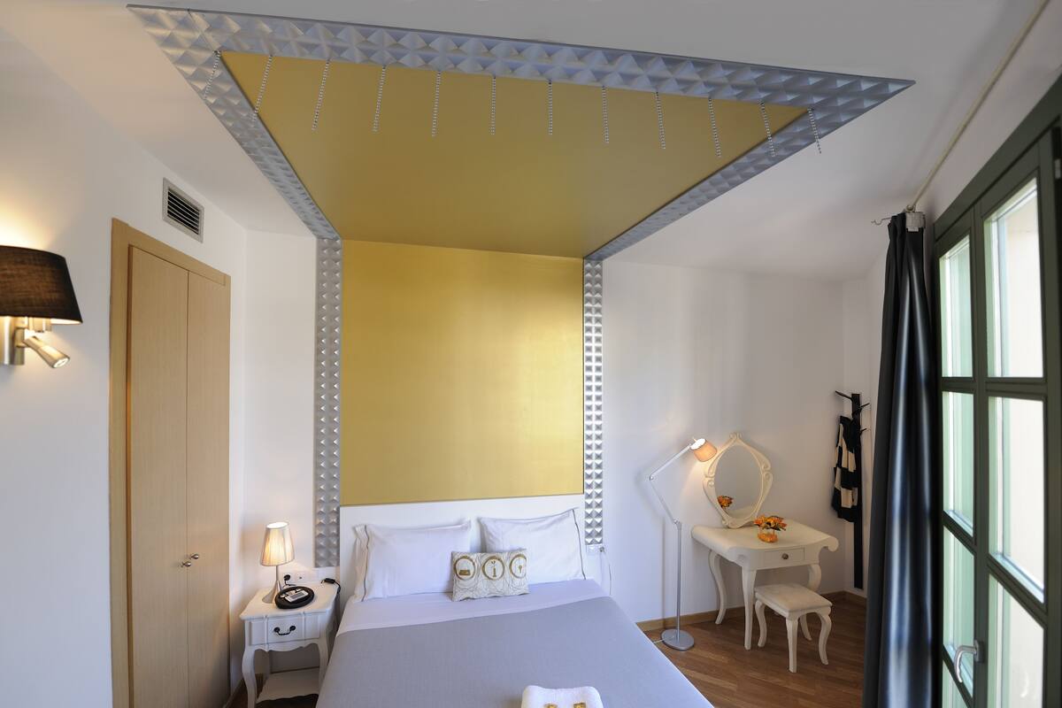 Un dormitorio con cama, mesita de noche, lámpara, cómoda, espejo y ventana.
