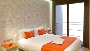 Habitación de hotel con cama, mesita de noche, control remoto y ventana con vistas.