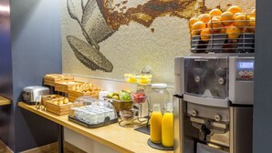 Un bufé de desayuno con diversas opciones de comida, un dispensador de jugo y una pared decorativa.