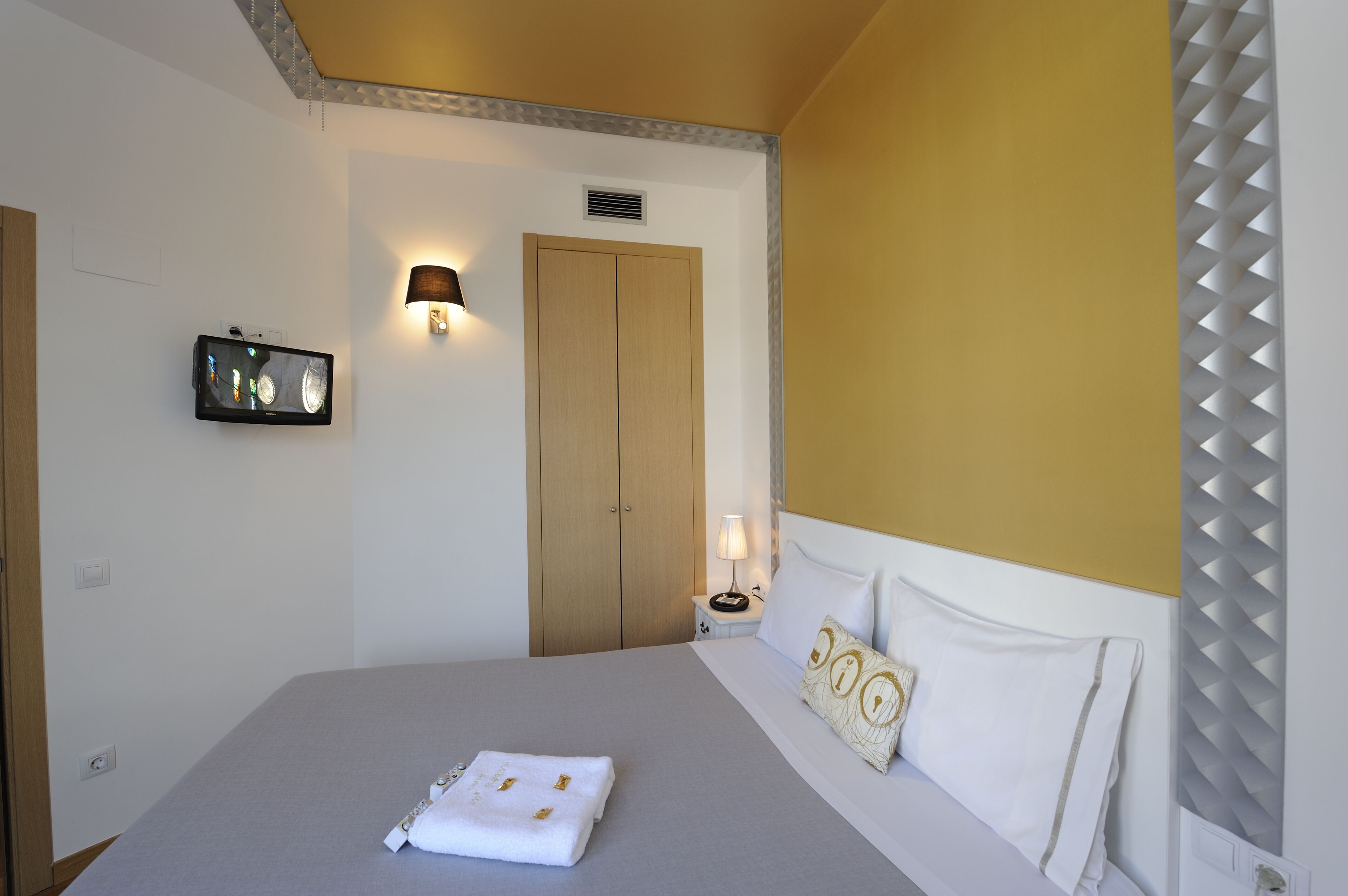 Ein ordentlich eingerichtetes Hotelzimmer mit Bett, Nachttischlampe, Wand-Fernseher und Tür.