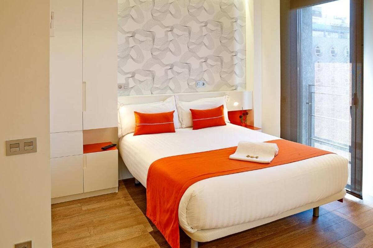 Una habitación de hotel moderna con una cama grande, ropa de cama blanca y detalles en naranja.