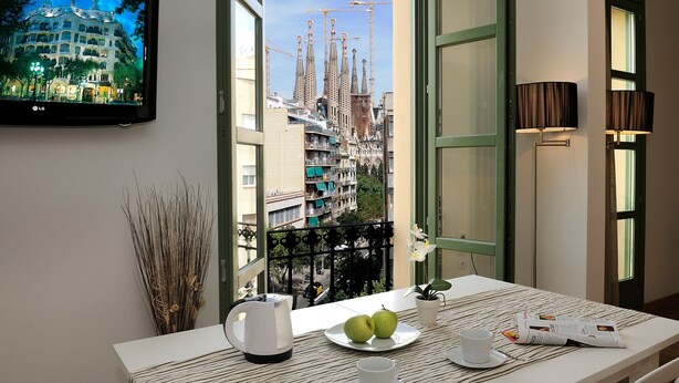 Habitación de hotel con balcón, una mesa con mantel a rayas, un plato con dos manzanas, una taza, un hervidor y una revista.