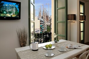 Habitación de hotel con balcón, una mesa con mantel a rayas, un plato con dos manzanas, una taza, un hervidor y una revista.