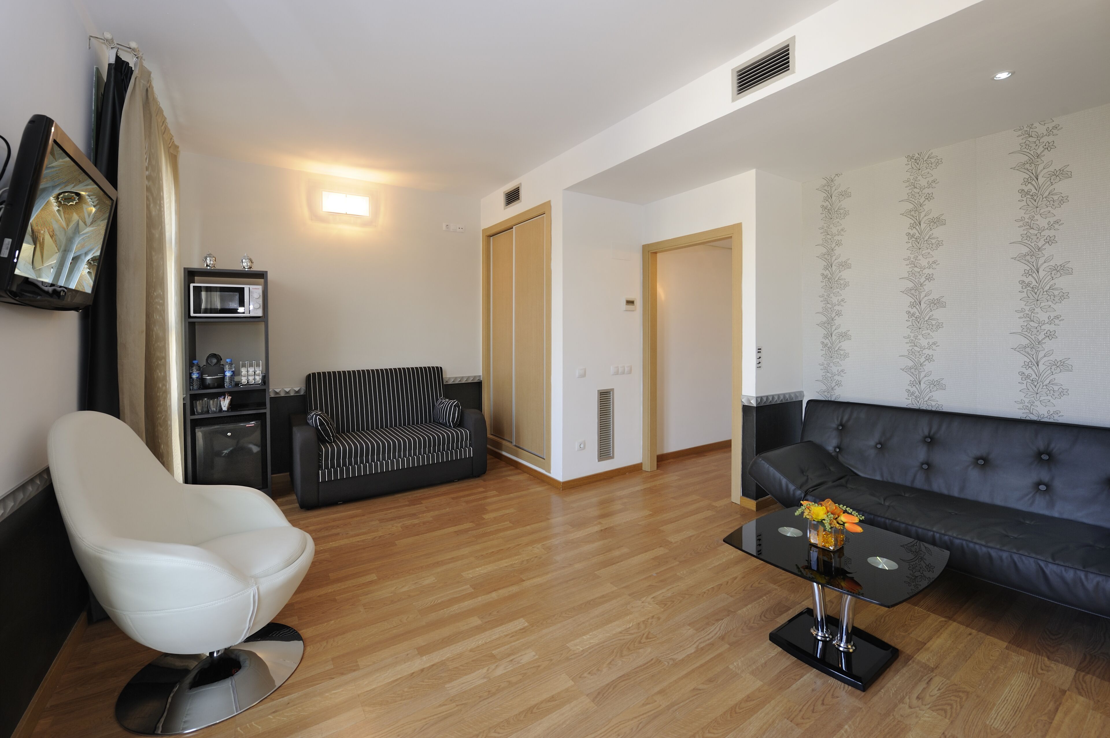 Un salon moderne avec un fauteuil blanc, un canapé noir, une table basse en verre et un four à micro-ondes.