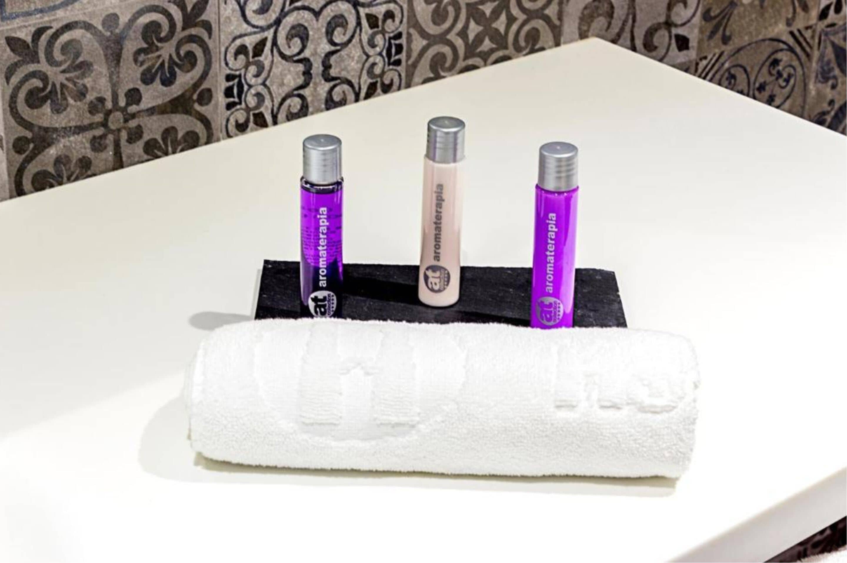 Un baño con un lavamanos blanco, tres frascos de productos de aromaterapia y una toalla blanca.