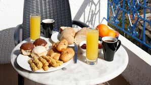 A balcony with a table set for breakfast, including croissants, pastries, and orange juice. - Atheras (Ikaria)