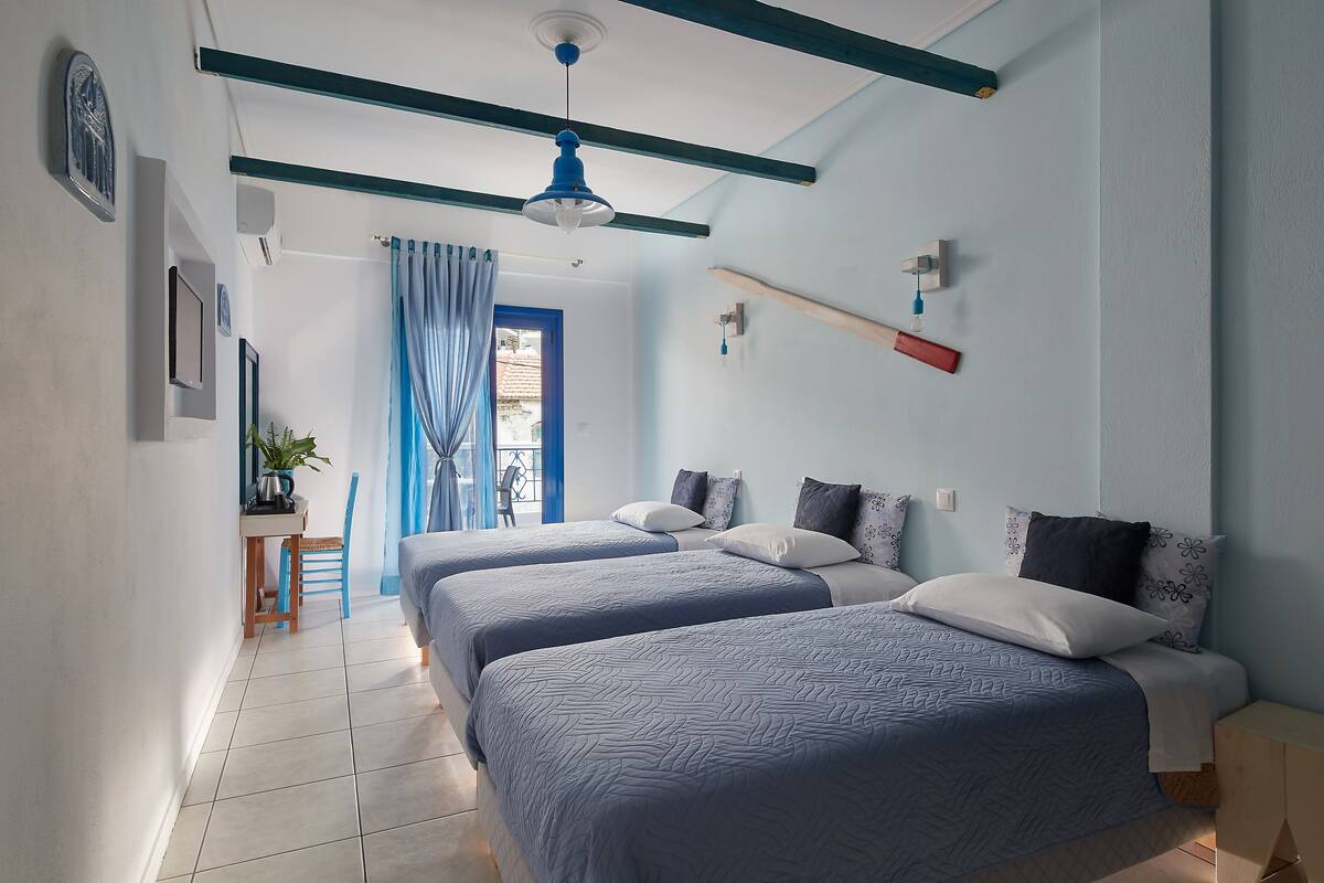 A bedroom with two beds, a desk with a chair, a window with blue curtains, and a ceiling fan.