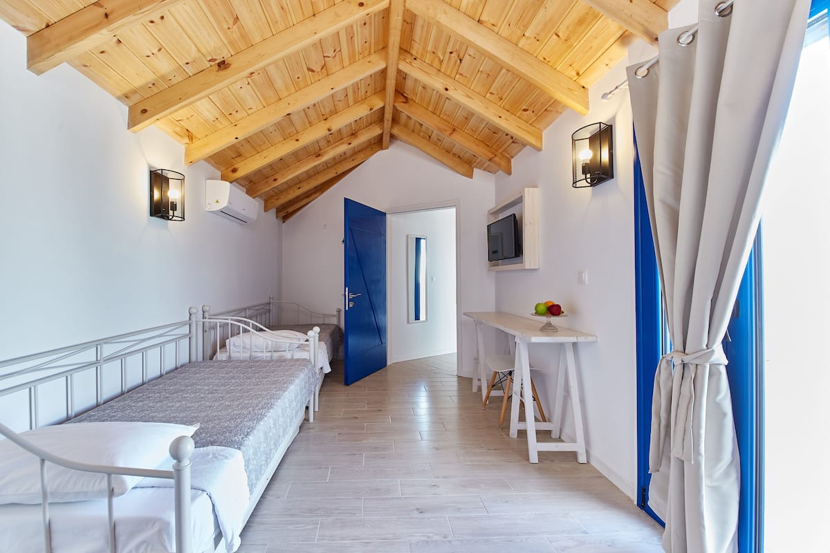 A bedroom with a sloped wooden ceiling, a bed, a desk, and a TV.
