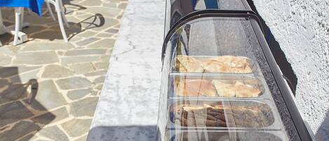 Un bufé con diferentes opciones de comida, piso de piedra y mesas al aire libre con mantel azul.