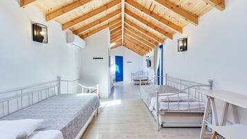 A modern room with a high wooden ceiling, two beds, a desk, and a blue door in the background.
