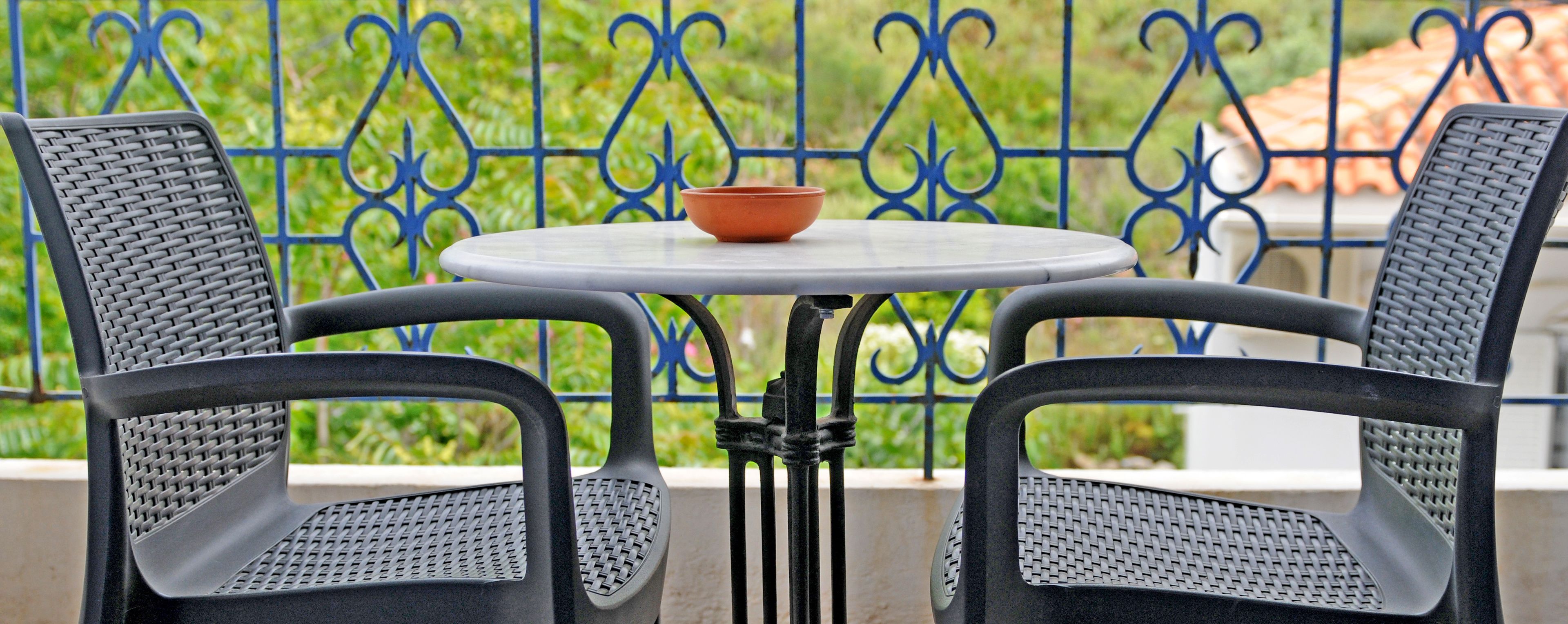A balcony with two black wicker chairs, a small round table, and a bowl.