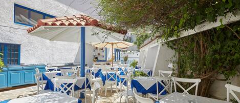 An outdoor dining area with white tables and chairs, blue tablecloths, and umbrellas.