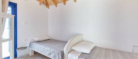 A bedroom with two single beds, a wooden ceiling, and a white wall.