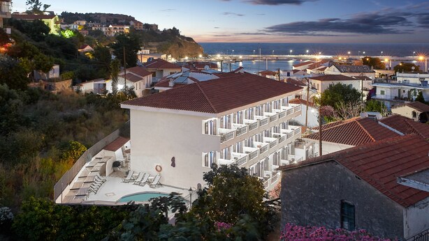 A coastal town with a prominent white building featuring balconies and a swimming pool. - Atheras (Ikaria)