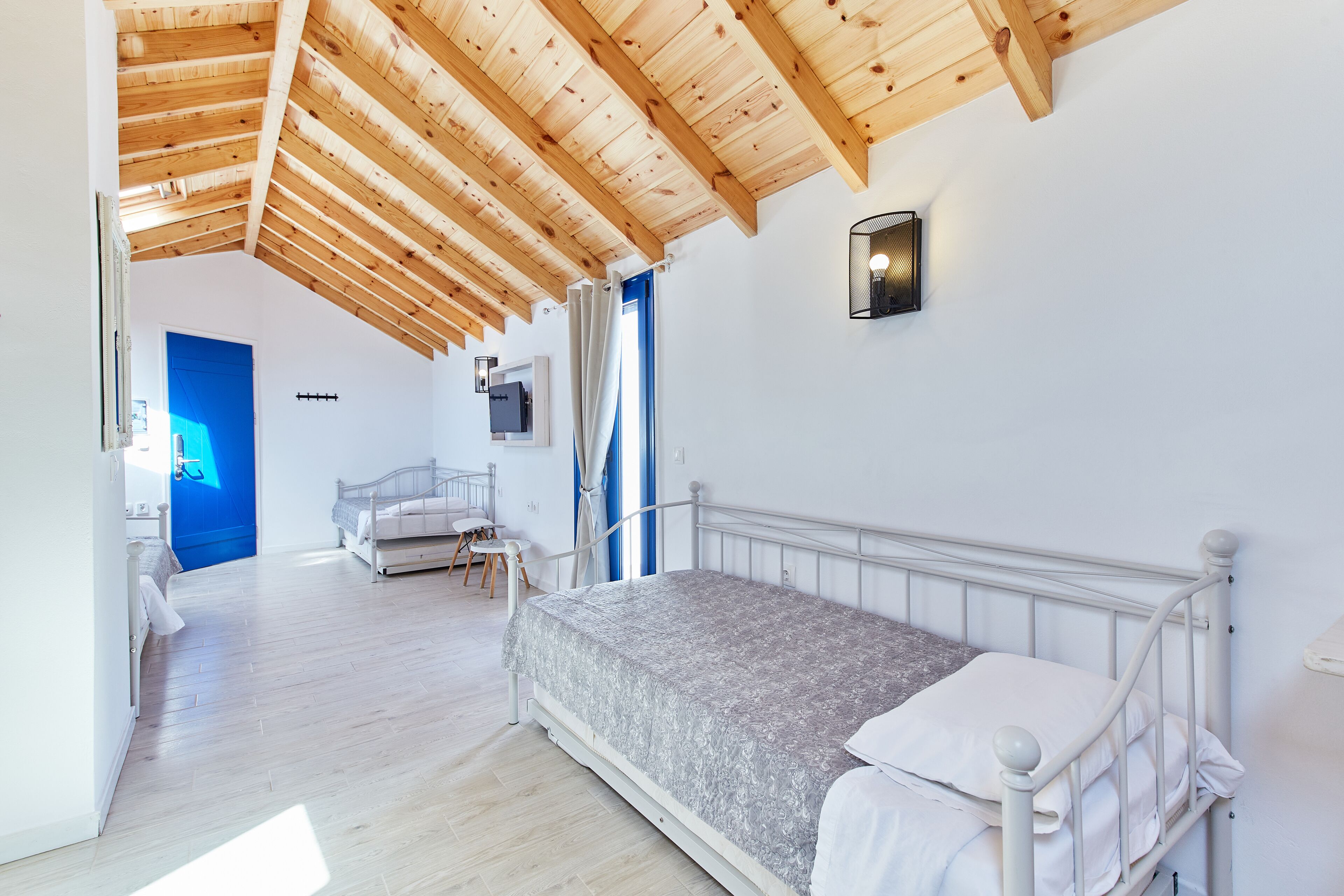 A bedroom with a wooden ceiling, a bed, a TV, and a bathroom in the background.