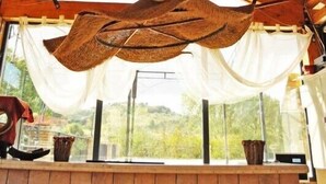 Un interior rústico con techo de madera, una lámpara colgante de fibras tejidas y vistas al verdor exterior.