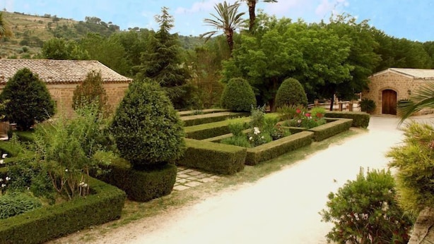 Un jardín con setos cuidados, un sendero y edificios de piedra.