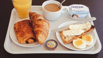 Una bandeja de desayuno con croissants, huevos, mantequilla, un vaso de zumo de naranja, una taza de café y un envase de yogur Danone.