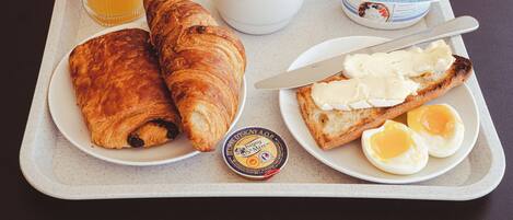 Een ontbijfwagen met croissants, eieren, boter, een glas sinaasappelsap, een kop koffie en een bakje Danone yoghurt.