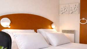 Una habitación de hotel con una cama, almohadas blancas, una mesita de noche roja y una planta en maceta.