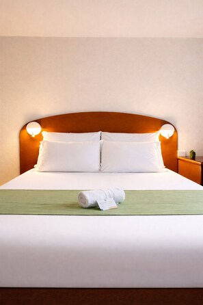 A neatly made bed with white linens, a wooden headboard with wall-mounted lights, and a green bed runner. - Quick Palace Montpellier (Saint-Jean-de-Vedas)
