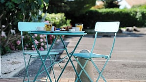 Juego de mesa y sillas metálicas turquesa al aire libre con base de piedra, una taza blanca, un vaso de jugo de naranja y un sándwich.