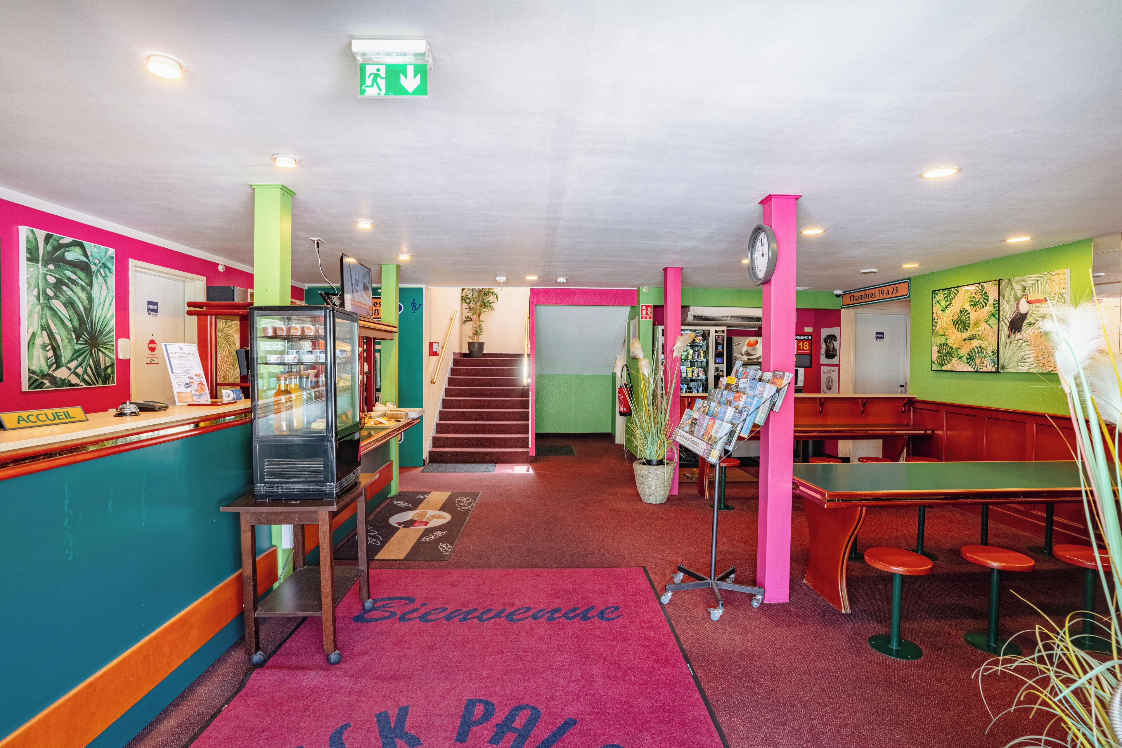 A brightly colored interior with a reception desk, a staircase, and a seating area.