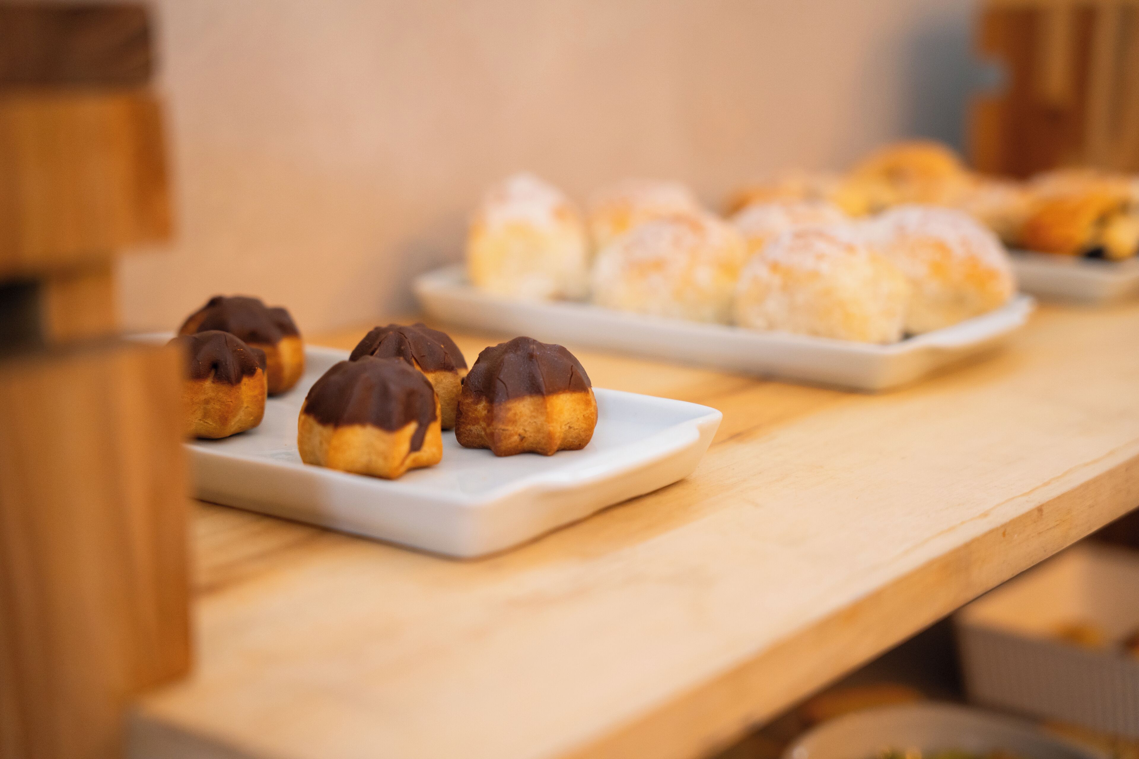 Uma variedade de doces sobre um prato branco, com um fundo desfocado que sugere um café.