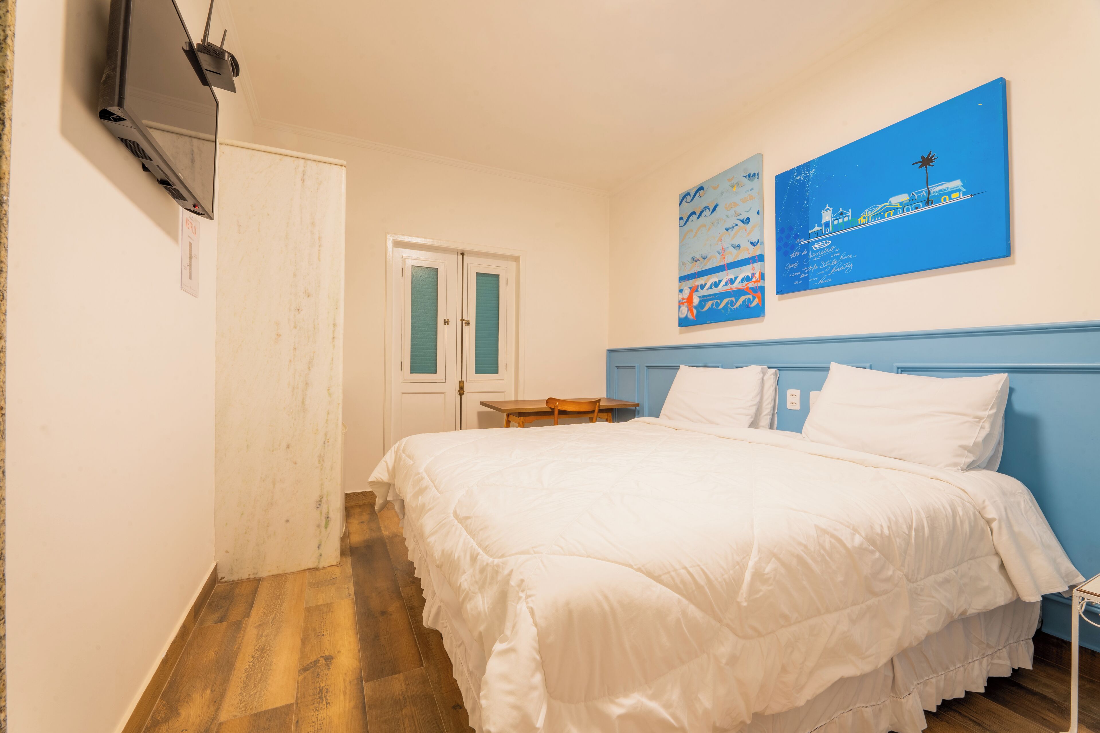 Un dormitorio con cama, escritorio y televisor montado en la pared.