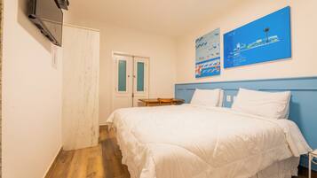 Un dormitorio con cama, escritorio y televisor montado en la pared.