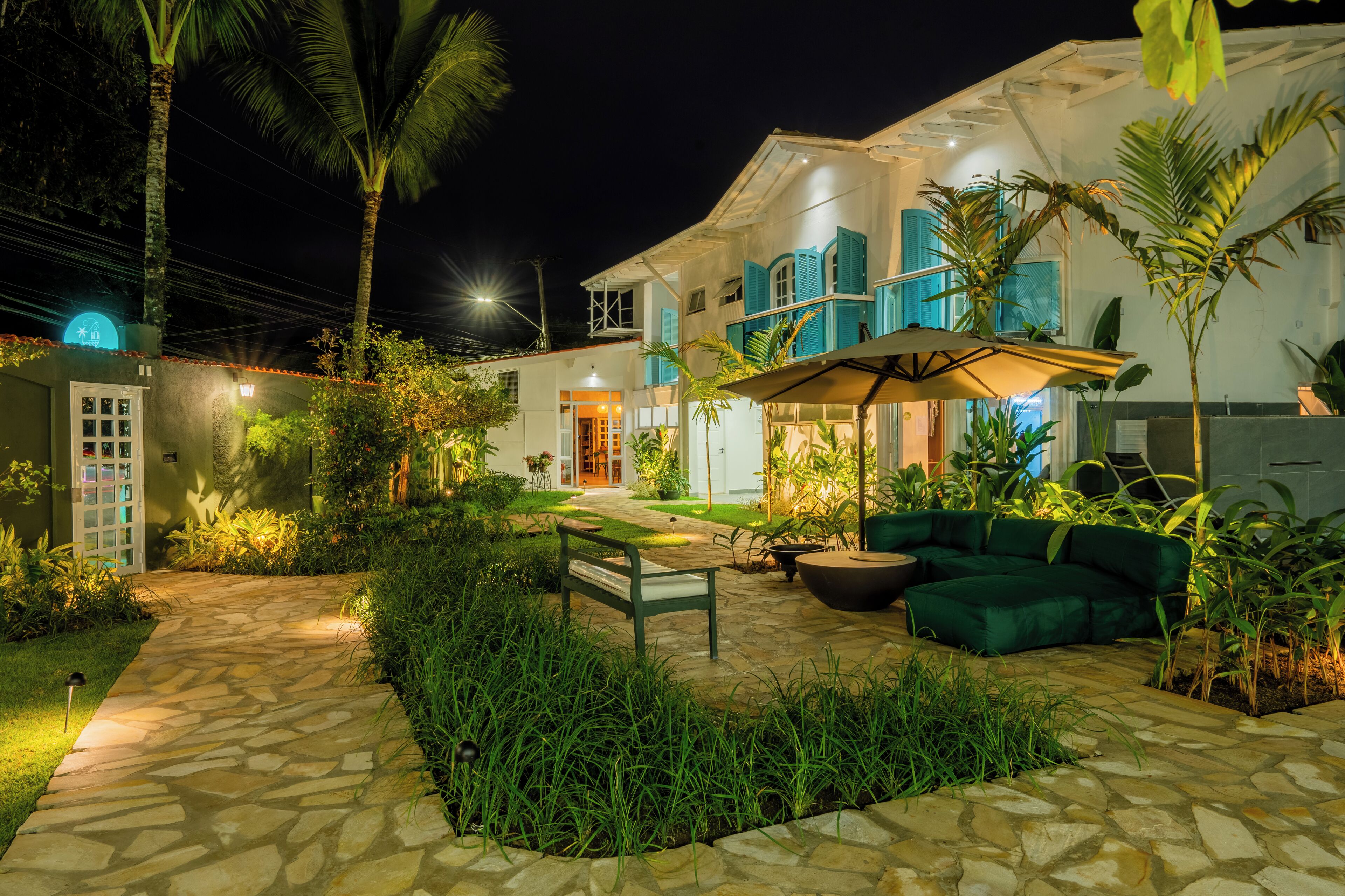 Un patio bien iluminado con un sendero de piedra, asientos verdes y plantas exuberantes.