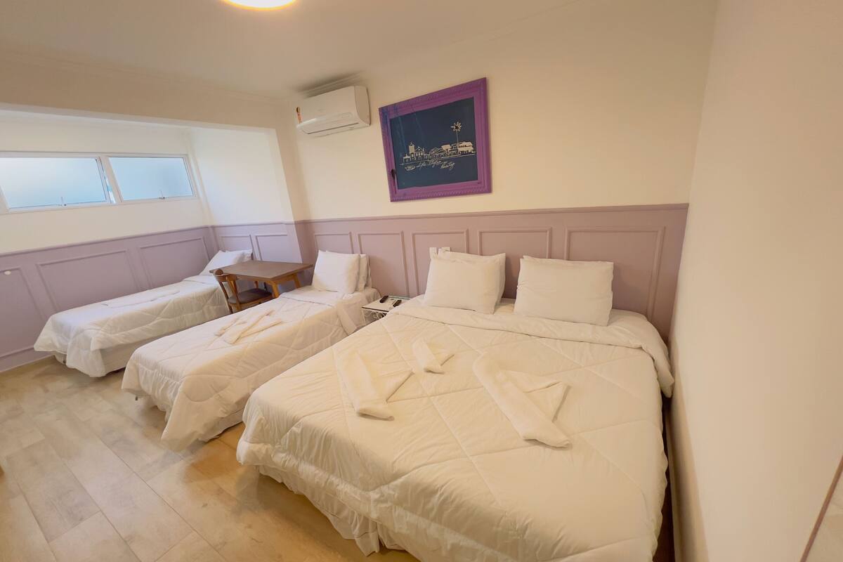 Hotellihuone, jossa on kaksi sänkyä, ikkuna, seinään asennettu ilmastointilaite ja kehystetty taulu.